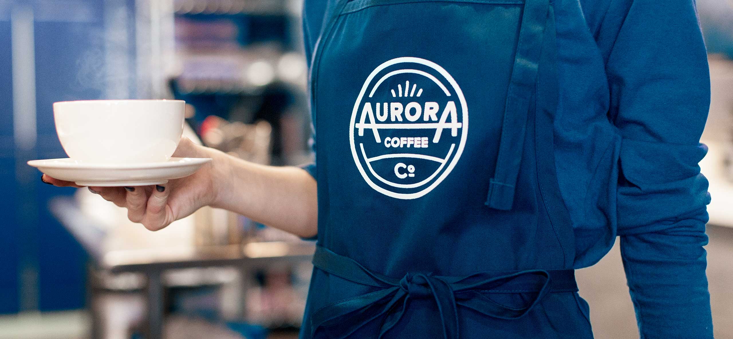 Aurora Barista holding coffee mug in apron